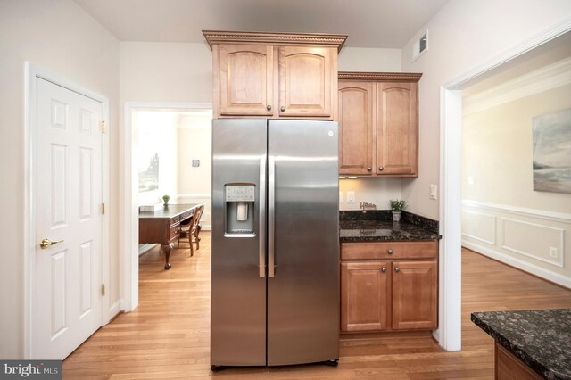 kitchen featuring stainless steel fridge with ice dispenser, dark stone counters, light wood-type flooring, and wainscoting