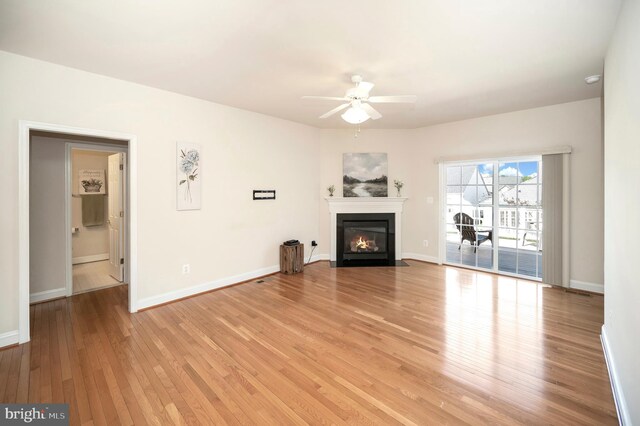 unfurnished living room with a fireplace with flush hearth, baseboards, light wood-style floors, and a ceiling fan