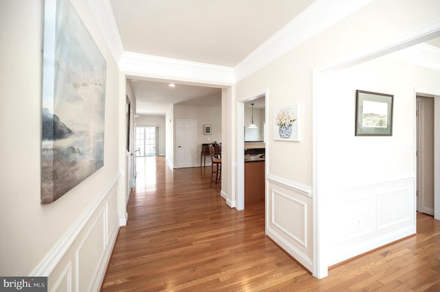 hallway featuring a wainscoted wall, a decorative wall, light wood-style flooring, and ornamental molding
