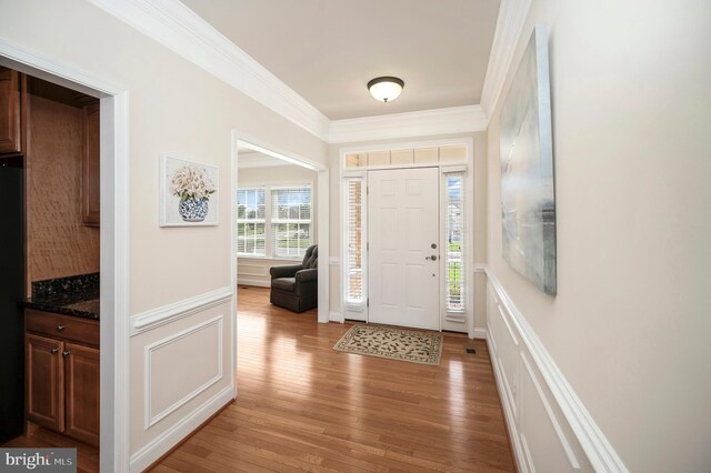 entryway featuring wainscoting, crown molding, light wood-style floors, and a decorative wall
