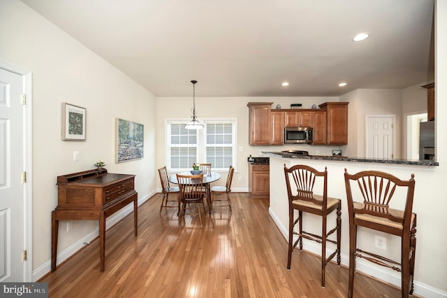 kitchen with light wood finished floors, a kitchen bar, hanging light fixtures, stainless steel appliances, and recessed lighting