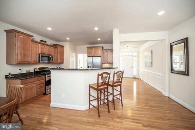 kitchen with light wood finished floors, a breakfast bar area, dark stone countertops, stainless steel appliances, and recessed lighting