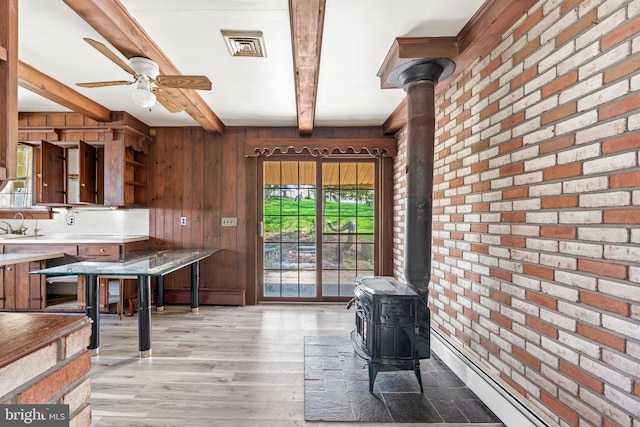 kitchen with wooden walls, a wood stove, a ceiling fan, beamed ceiling, and brick wall