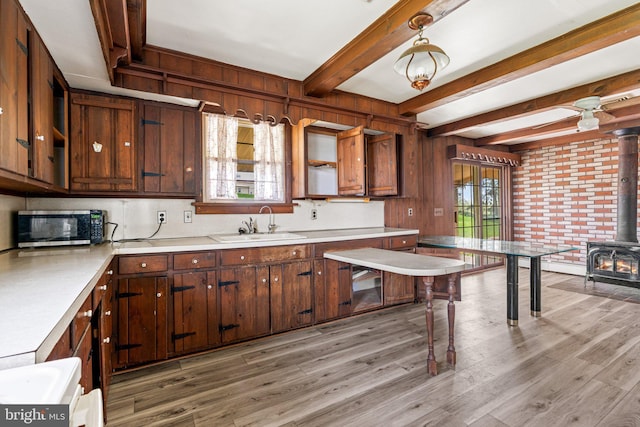 kitchen featuring light wood finished floors, light countertops, a wood stove, a sink, and stainless steel microwave