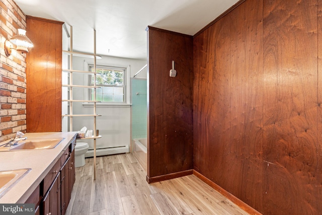 full bath with a sink, double vanity, toilet, wood finished floors, and a baseboard radiator