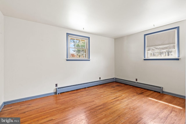 unfurnished room with a baseboard radiator, wood finished floors, and baseboards