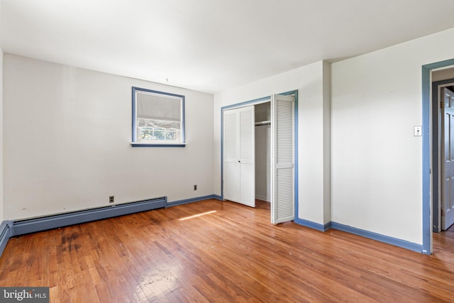 unfurnished bedroom featuring baseboards, wood finished floors, a closet, and baseboard heating
