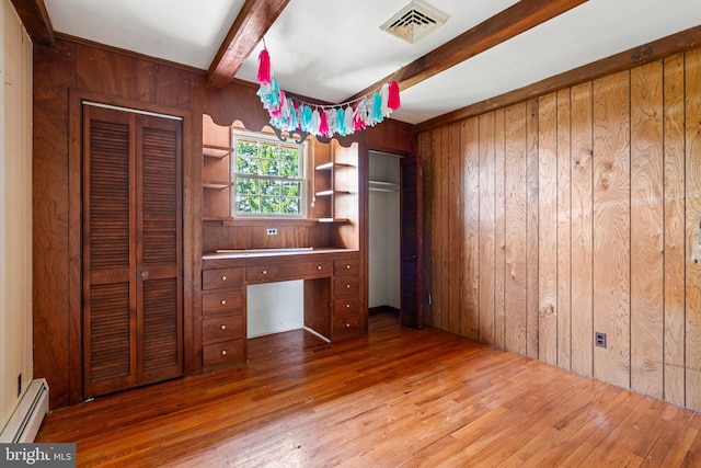 unfurnished bedroom featuring a baseboard radiator, wood-type flooring, visible vents, and wood walls