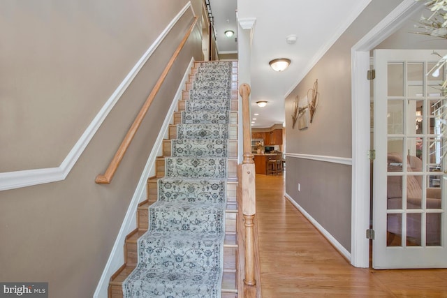 stairway with ornamental molding, baseboards, and wood finished floors