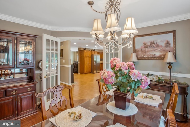 dining space with light wood finished floors, an inviting chandelier, and crown molding