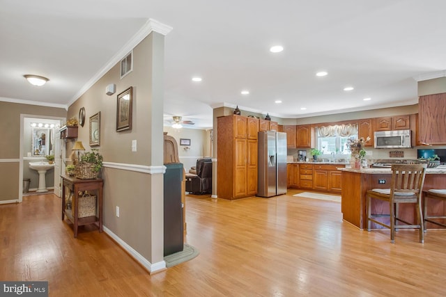 kitchen featuring light wood-style flooring, a breakfast bar, brown cabinetry, appliances with stainless steel finishes, and ornamental molding