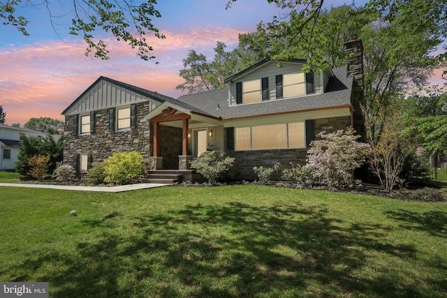 split level home with a chimney, board and batten siding, a lawn, and stone siding
