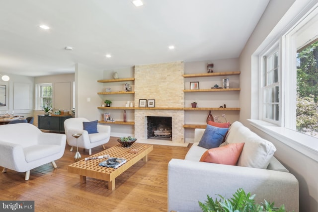 living area with recessed lighting, light wood finished floors, and a stone fireplace