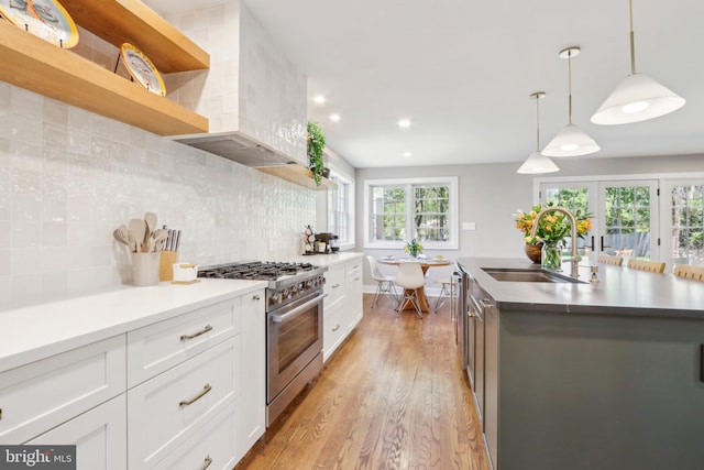 kitchen with light wood-style floors, wall chimney exhaust hood, white cabinetry, a sink, and appliances with stainless steel finishes