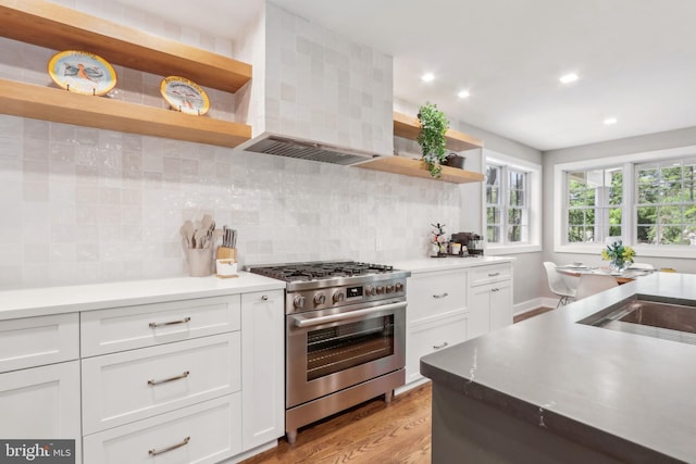 kitchen with open shelves, wall chimney exhaust hood, stainless steel gas stove, and white cabinetry