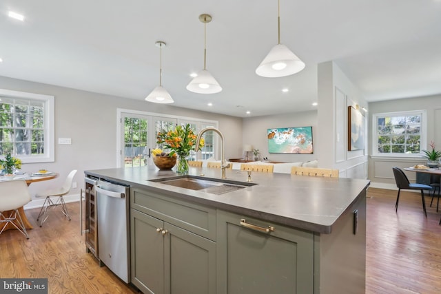 kitchen featuring stainless steel dishwasher, an island with sink, plenty of natural light, light wood-type flooring, and a sink
