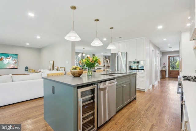 kitchen featuring white cabinets, appliances with stainless steel finishes, a sink, beverage cooler, and open floor plan