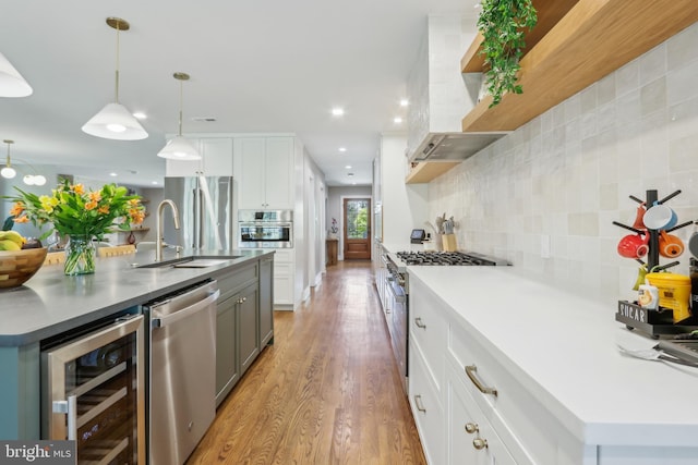 kitchen with beverage cooler, wall chimney exhaust hood, tasteful backsplash, a sink, and stainless steel appliances