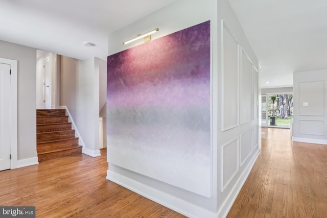 corridor featuring baseboards, stairs, and wood finished floors
