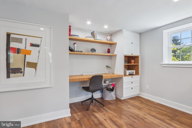 office space featuring baseboards, recessed lighting, built in desk, and wood finished floors