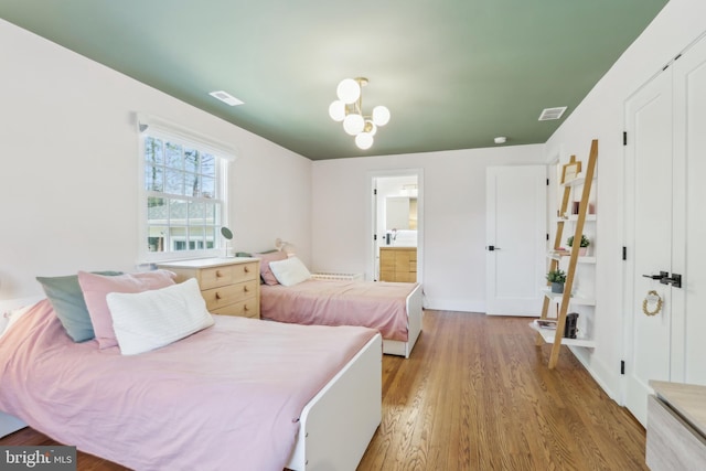 bedroom featuring light wood-style floors, baseboards, ensuite bath, and visible vents