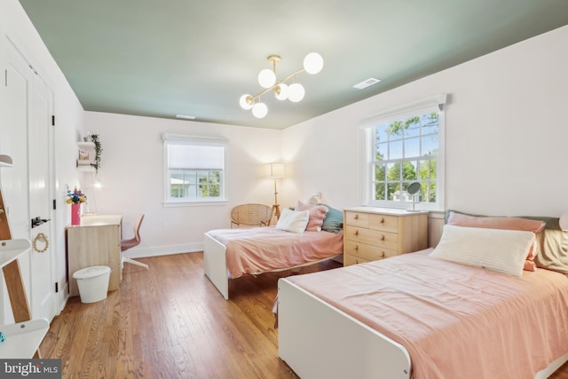 bedroom with an inviting chandelier, multiple windows, light wood-style floors, and visible vents