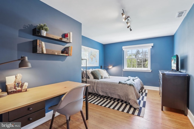 bedroom with visible vents, baseboards, wood finished floors, and track lighting