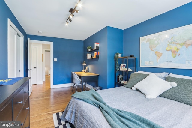 bedroom with baseboards, track lighting, and wood finished floors