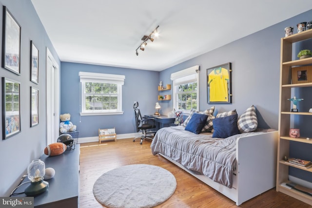 bedroom with track lighting, multiple windows, and wood finished floors