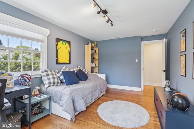 bedroom with baseboards, track lighting, and wood finished floors