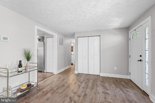 entryway with wood finished floors, a textured ceiling, baseboards, and visible vents