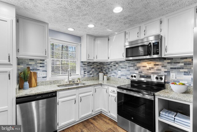 kitchen featuring dark wood-style floors, a textured ceiling, a sink, white cabinetry, and appliances with stainless steel finishes