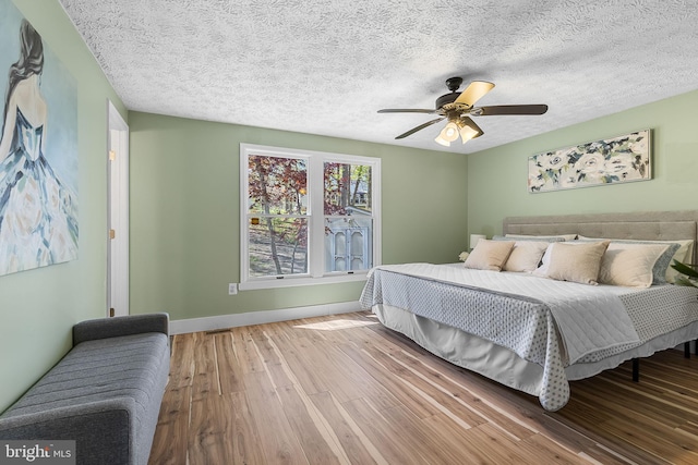 bedroom featuring ceiling fan, baseboards, wood finished floors, and a textured ceiling