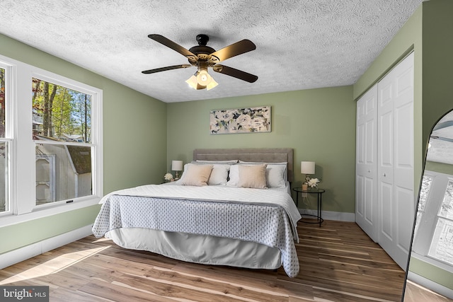 bedroom with a textured ceiling, baseboards, a ceiling fan, wood finished floors, and a closet