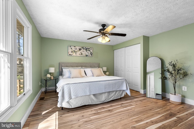bedroom featuring light wood-style floors, baseboards, a textured ceiling, and a closet