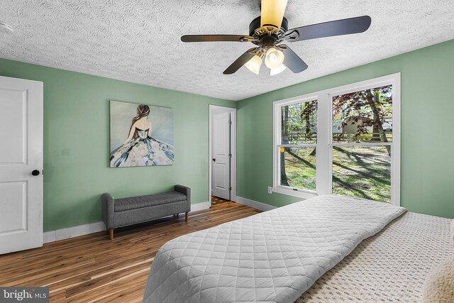 bedroom featuring wood finished floors, a textured ceiling, a ceiling fan, and baseboards