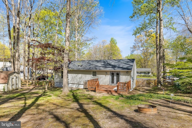 rear view of property featuring a storage shed, a shingled roof, french doors, an outdoor structure, and a wooden deck