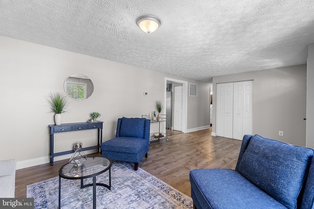 sitting room with a textured ceiling, wood finished floors, visible vents, and baseboards