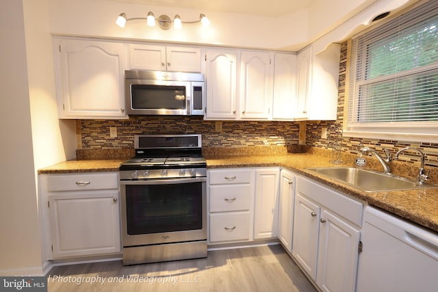 kitchen featuring stainless steel appliances, white cabinets, a sink, and backsplash