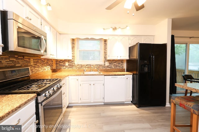 kitchen featuring stainless steel appliances, a sink, white cabinets, light wood-type flooring, and decorative backsplash