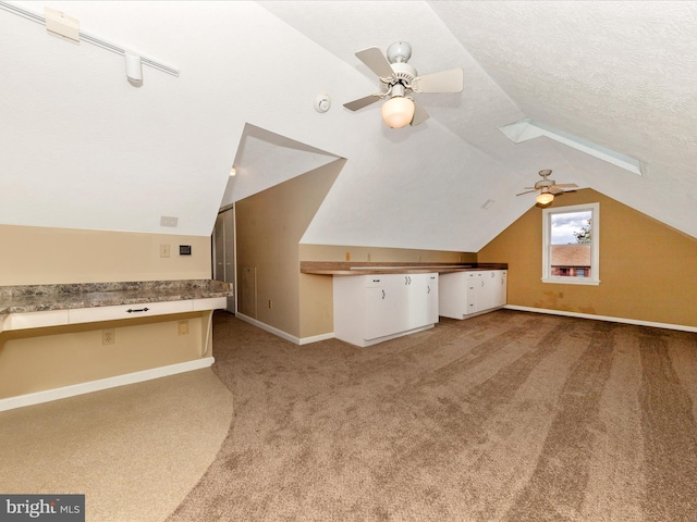 additional living space with built in desk, baseboards, a ceiling fan, lofted ceiling, and carpet