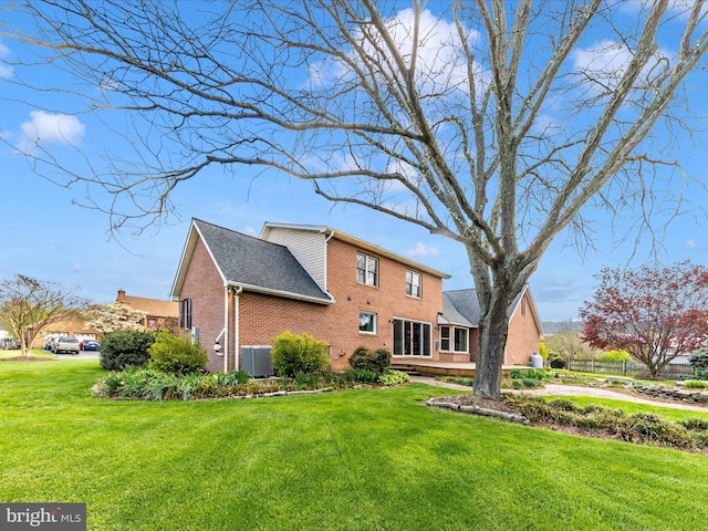 back of house featuring central air condition unit, brick siding, and a lawn