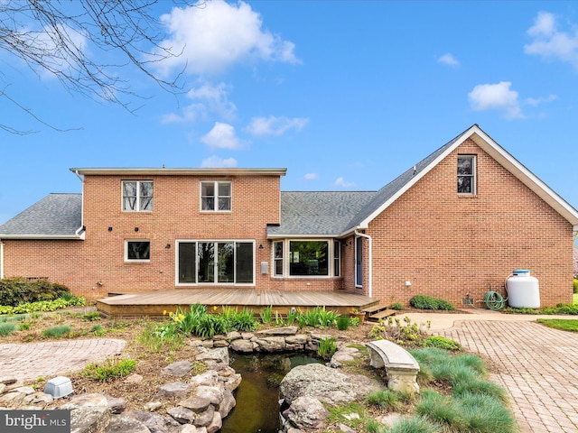 back of house featuring brick siding, a deck, and a shingled roof