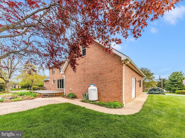 view of side of home with a yard, a deck, and brick siding