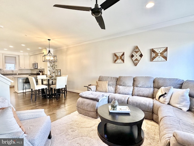 living room featuring recessed lighting, baseboards, ceiling fan with notable chandelier, crown molding, and wood finished floors