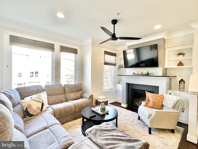 living room featuring baseboards, ornamental molding, a glass covered fireplace, ceiling fan, and wood finished floors