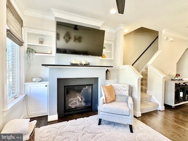 sitting room with recessed lighting, dark wood-style flooring, ornamental molding, a glass covered fireplace, and stairway