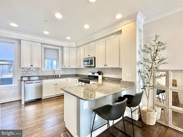 kitchen featuring a peninsula, a sink, stainless steel appliances, white cabinetry, and ornamental molding