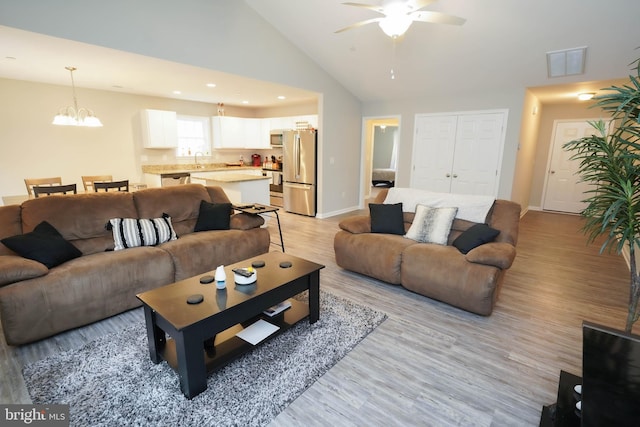 living room with ceiling fan with notable chandelier, baseboards, light wood finished floors, and visible vents