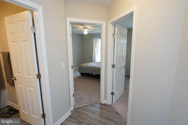 hallway featuring dark wood-style floors, dark carpet, and baseboards